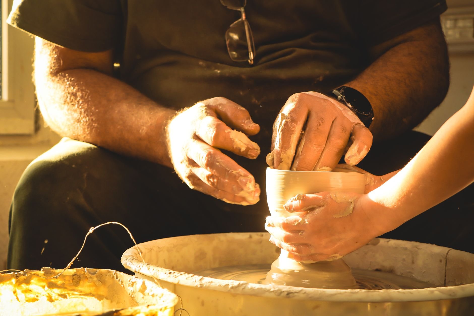 Close-up of hands molding clay on a potter's wheel, illuminated by warm sunlight.