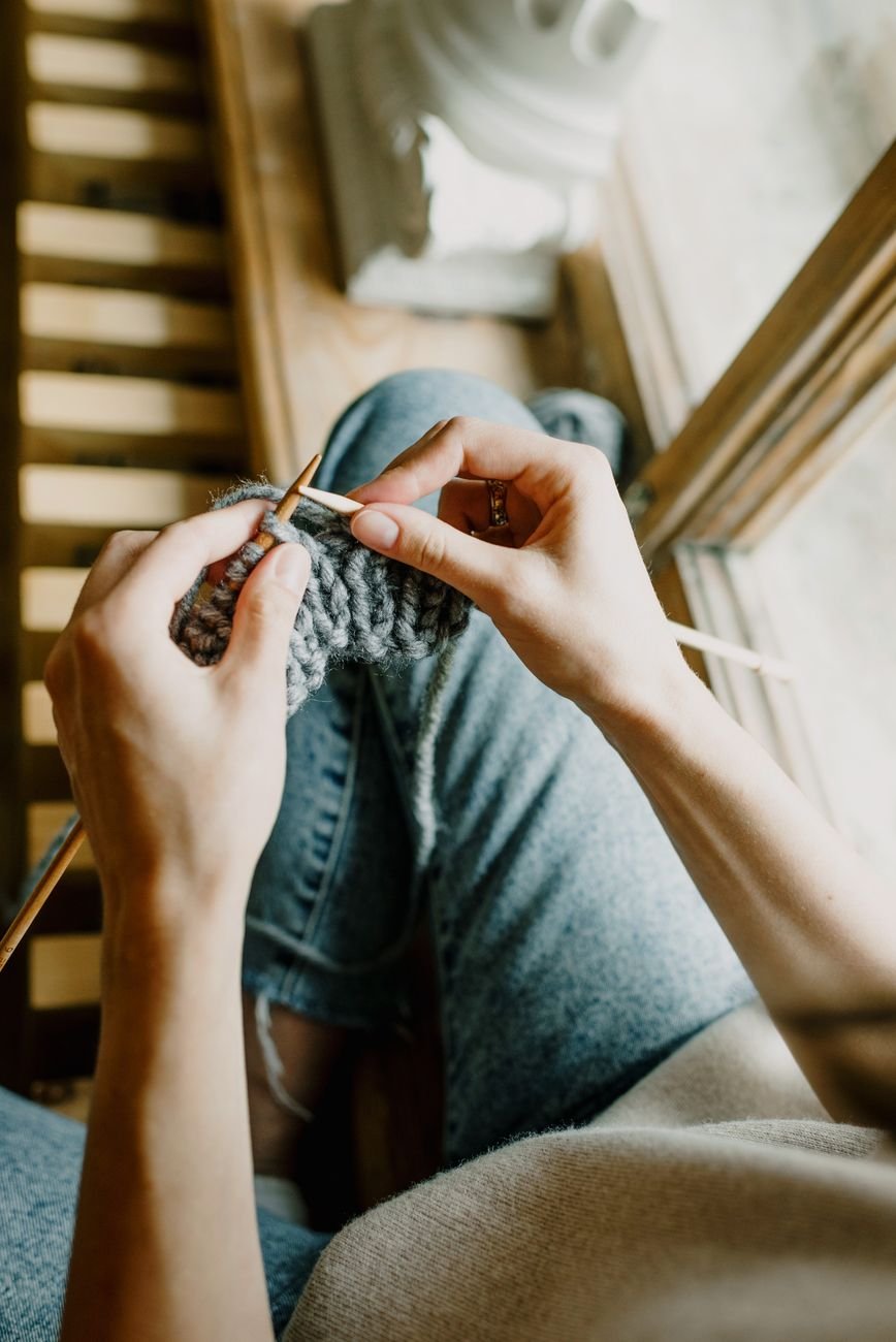 Hands knitting wool, a relaxing hobby enjoyed by a sunny window.